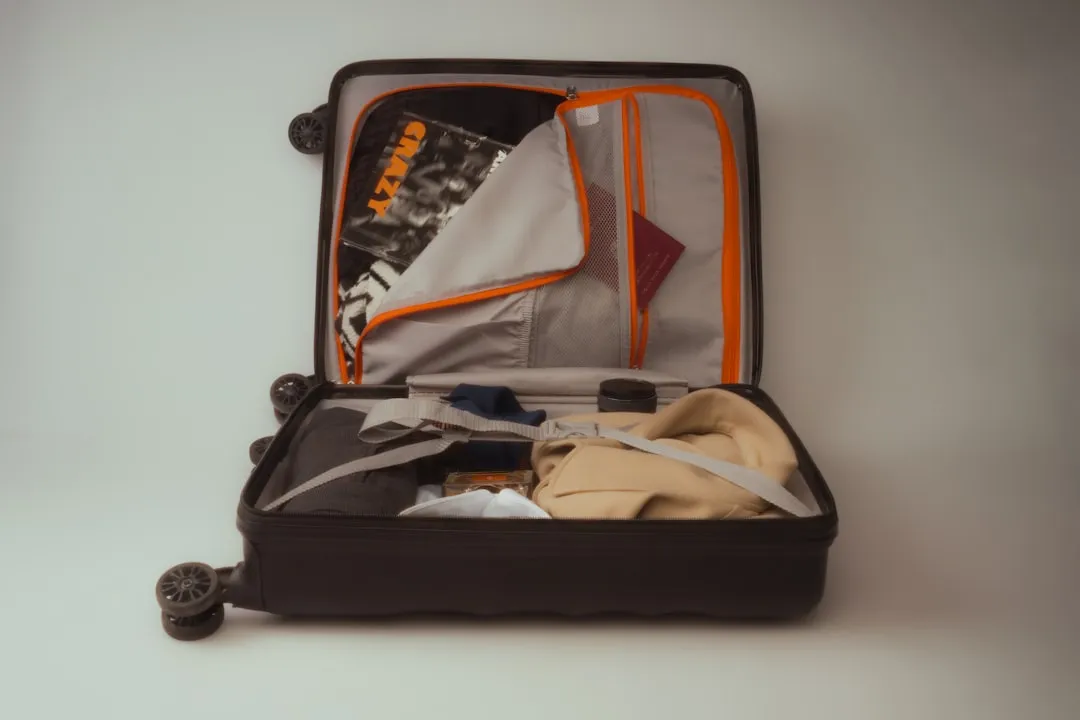 An open hard-shell suitcase holding folded clothes and a passport.