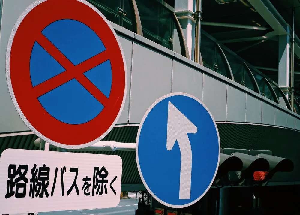 Japanese road signs mounted on a pole, including a no-stopping sign and a blue keep-left arrow.