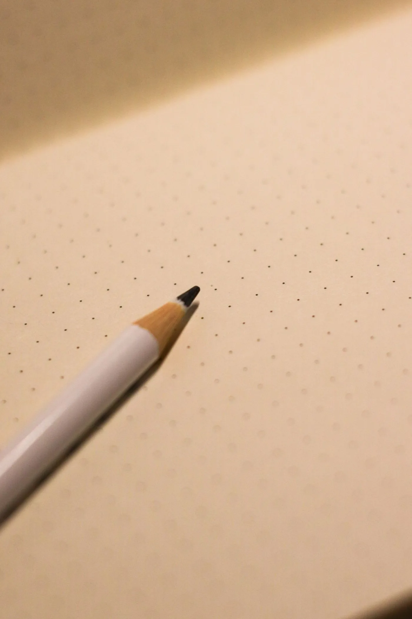 The sharpened tip of a pencil resting on the blank dotted page of an open notebook.