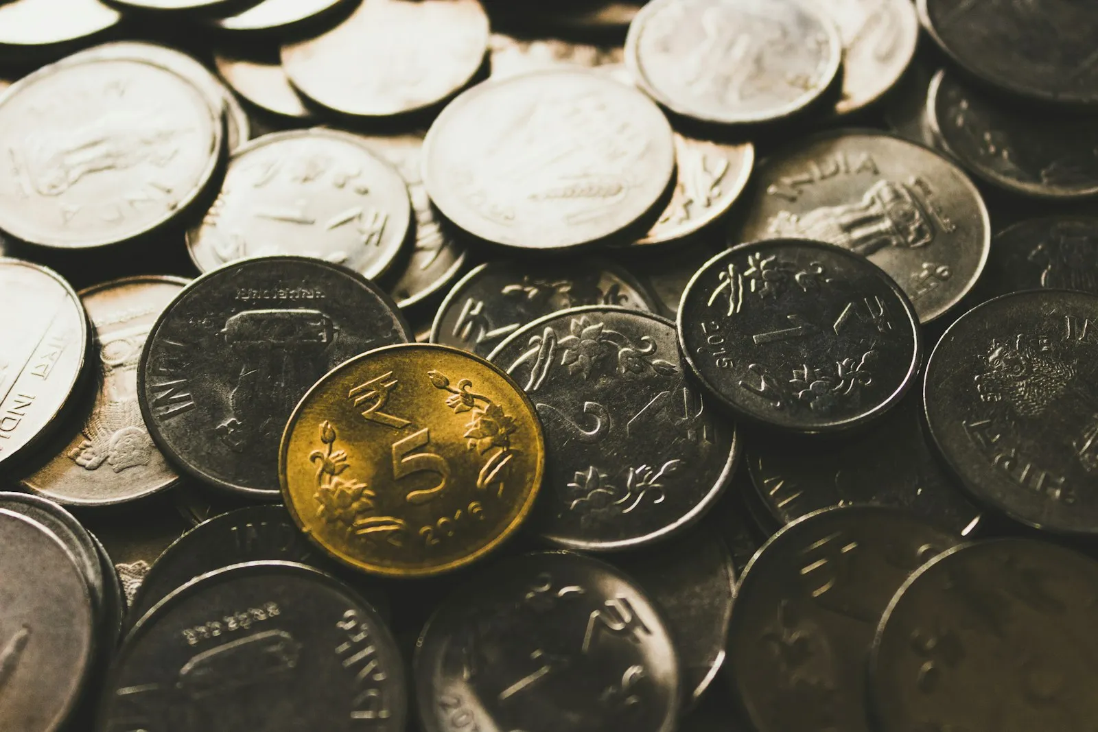 A close-up of a pile of coins with one gold-coloured coin among them.