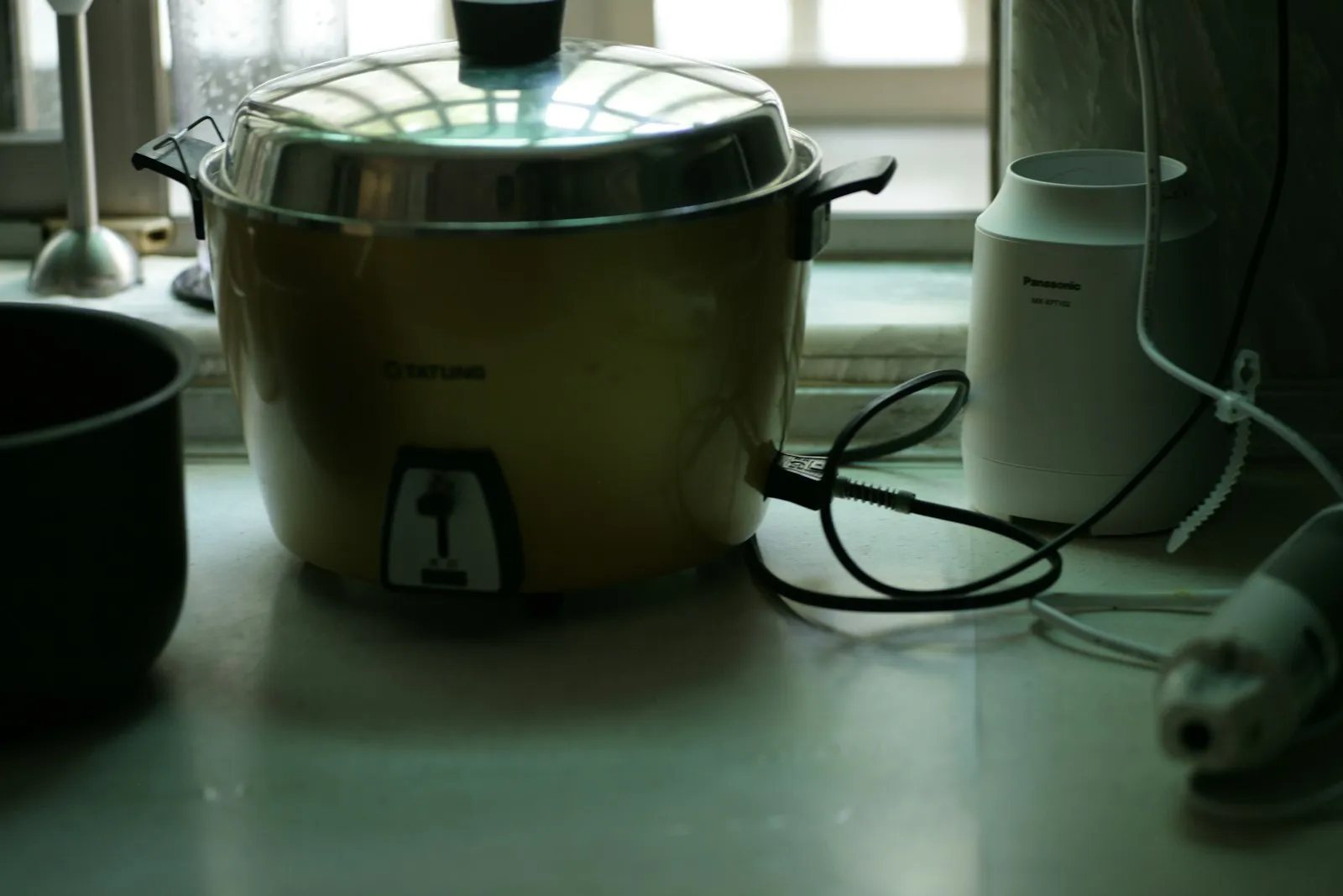 A rice cooker on a kitchen counter with its power cord coiled beside it.