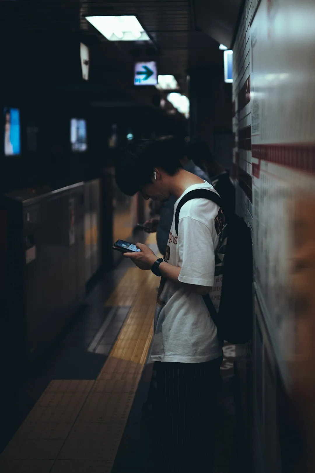 A person checking a smartphone while standing on a subway station platform in Tokyo.