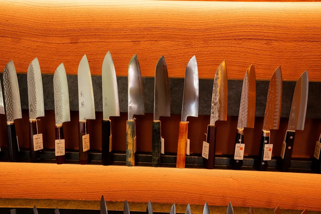 A row of Japanese kitchen knives with varied blade profiles and yen price tags on a wooden shop display.