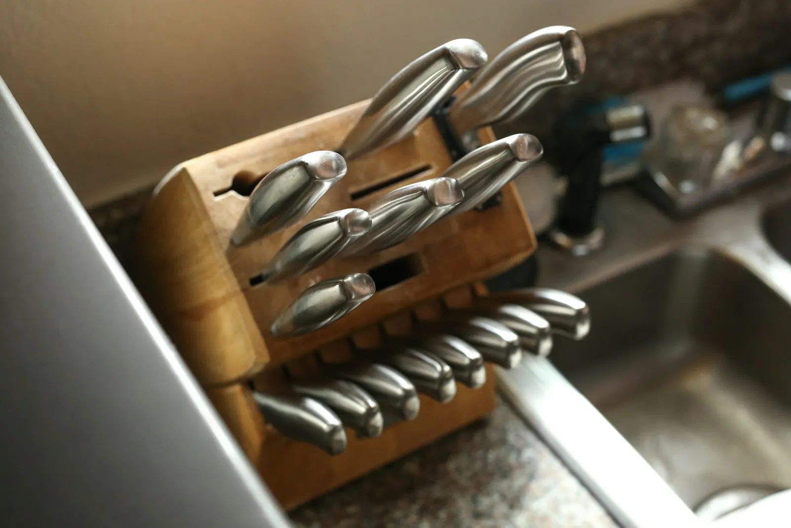 A wooden knife block holding a set of kitchen knives beside a sink.