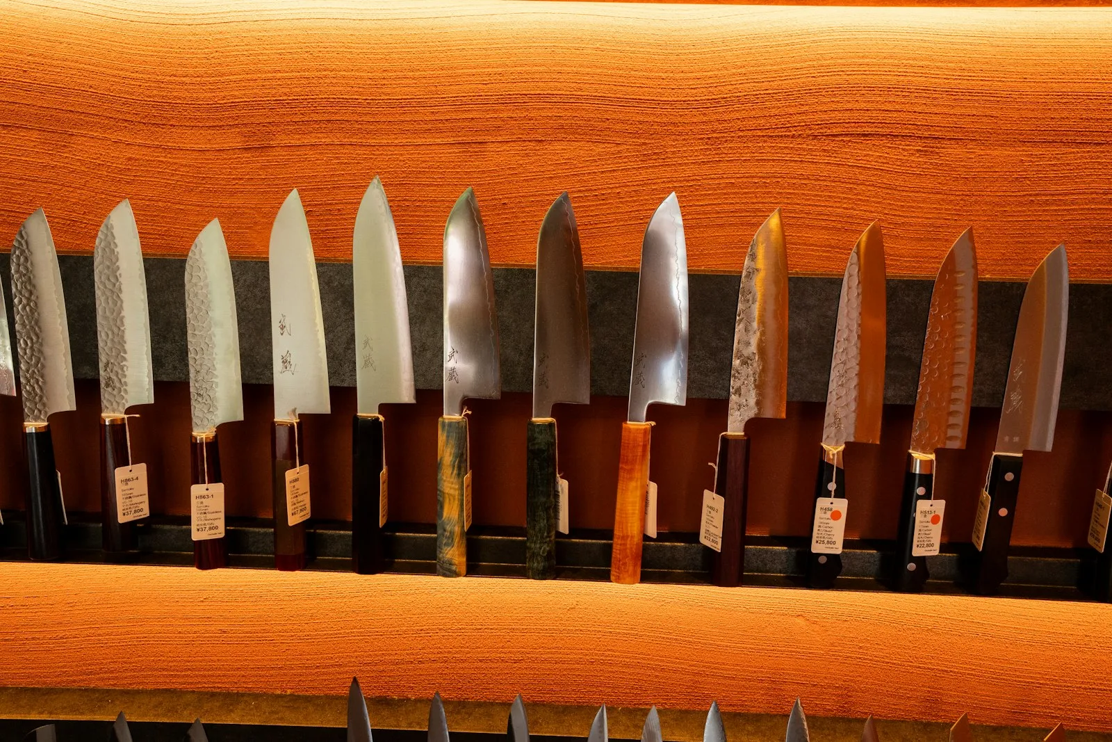 A row of Japanese kitchen knives displayed on a shop shelf.