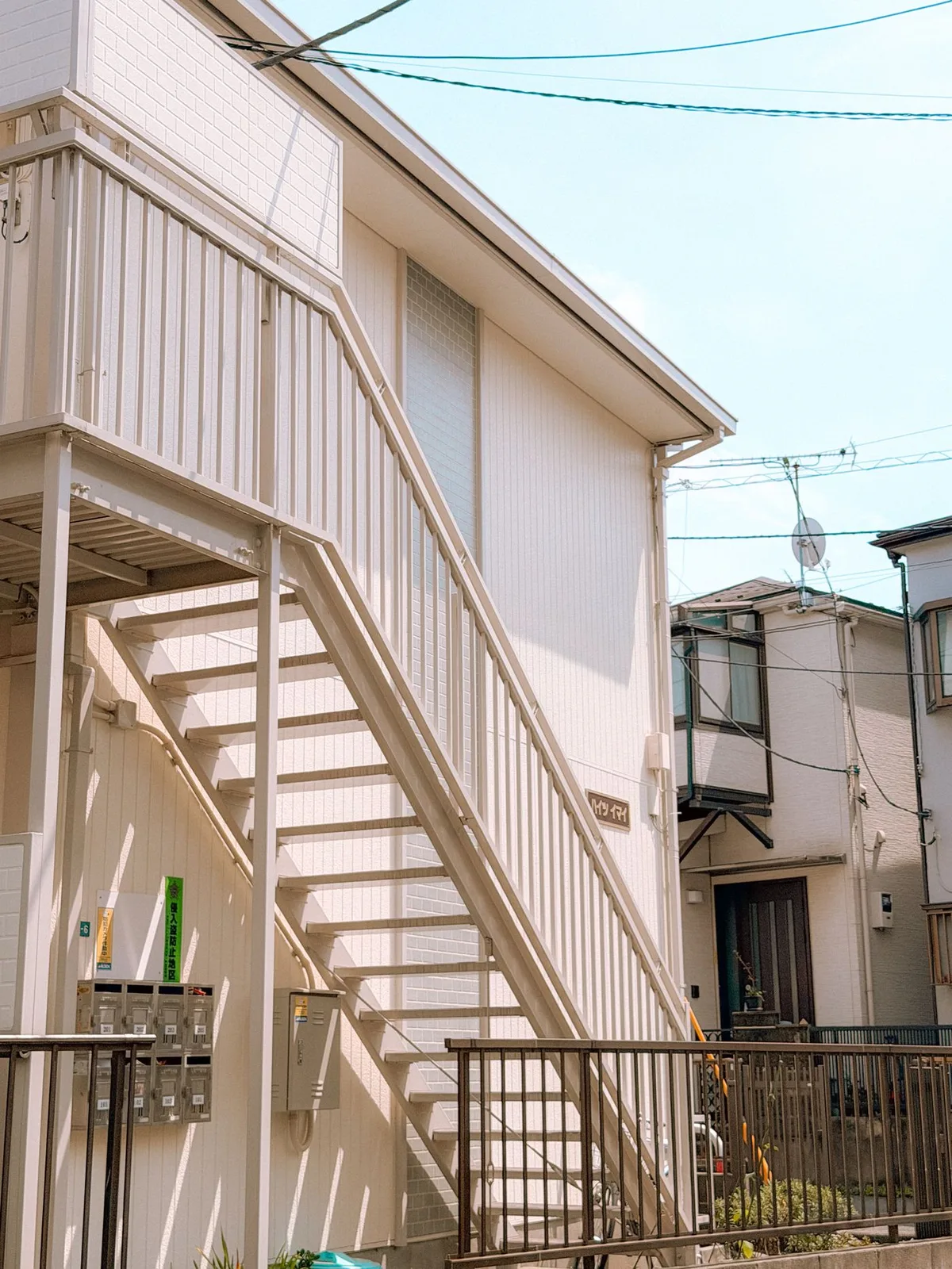 A two-storey Japanese apartment building with an external metal staircase and a bank of mailboxes below it.