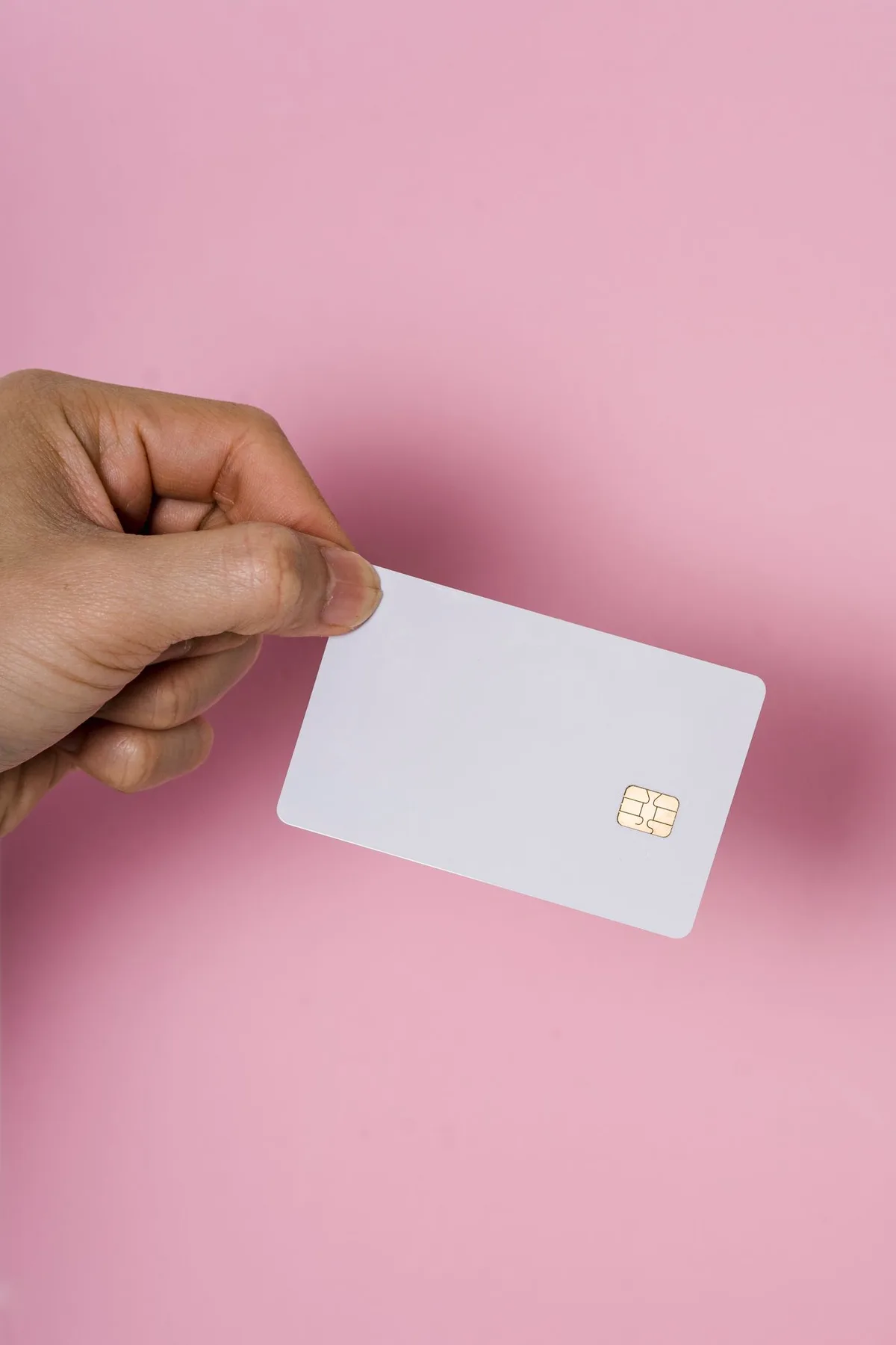 A hand holding a blank white chip card against a plain pink background.