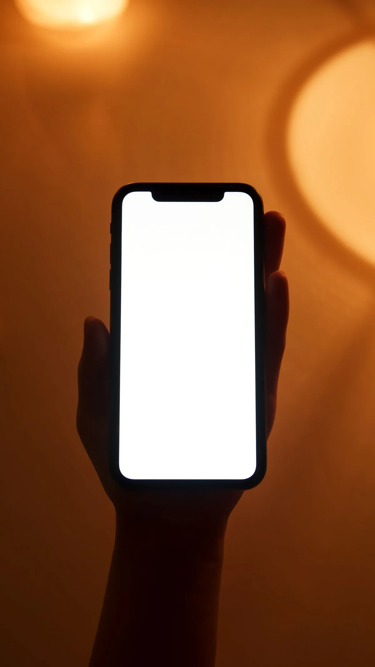 A hand holding a smartphone with a blank white screen against a warm orange background.