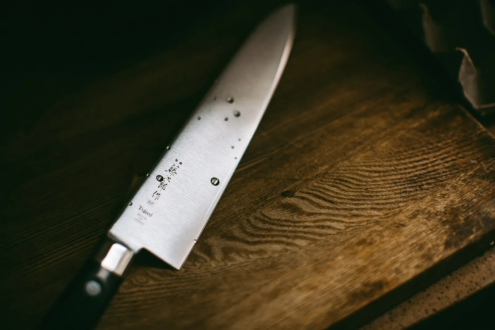 A Japanese chef knife with kanji on the blade resting on a dark wooden surface.