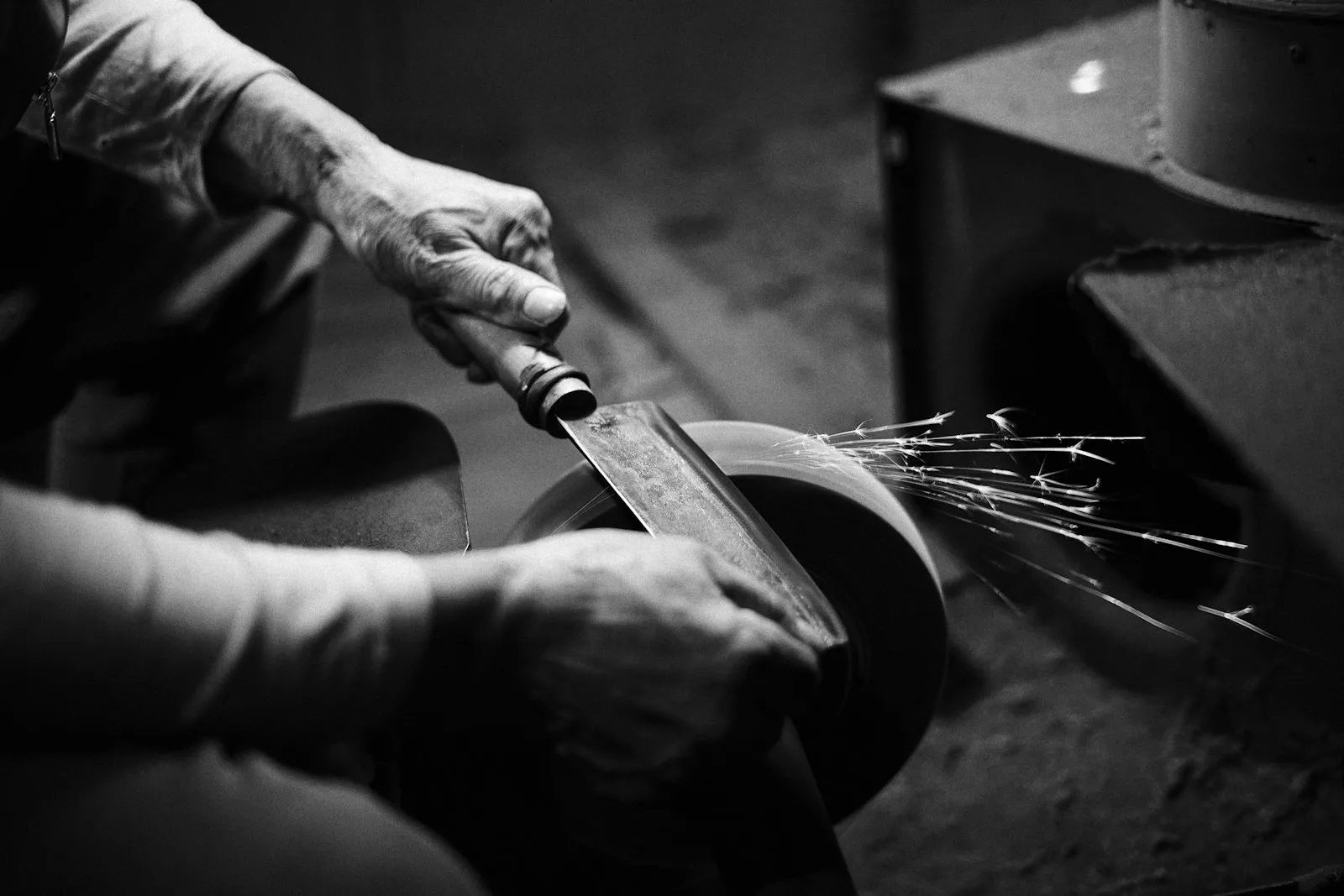 A worker grinding a blade against a spinning wheel, throwing sparks.
